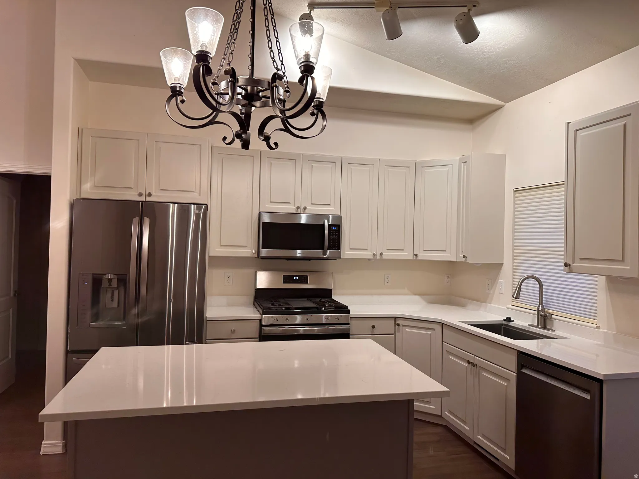 Bright kitchen featuring white cabinetry, light-toned countertops, stainless steel appliances, and a central island
