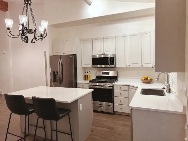 Modern kitchen featuring wood-finish flooring, white cabinetry, stainless steel appliances, a kitchen island with seating, and white countertops