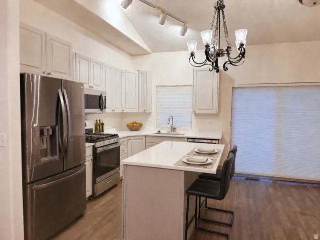 Kitchen featuring stainless steel appliances, wood-finish flooring, white cabinetry, a kitchen island with seating, and a decorative chandelier