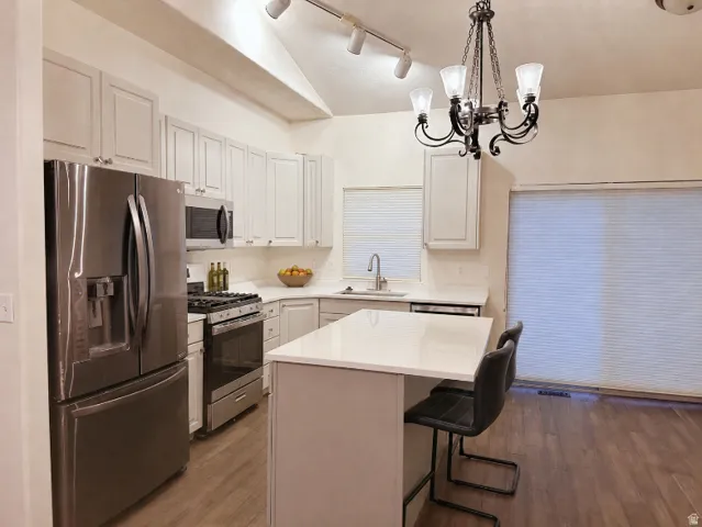Kitchen featuring stainless steel appliances, white cabinetry, white countertops, wood-finish flooring, and a vaulted ceiling