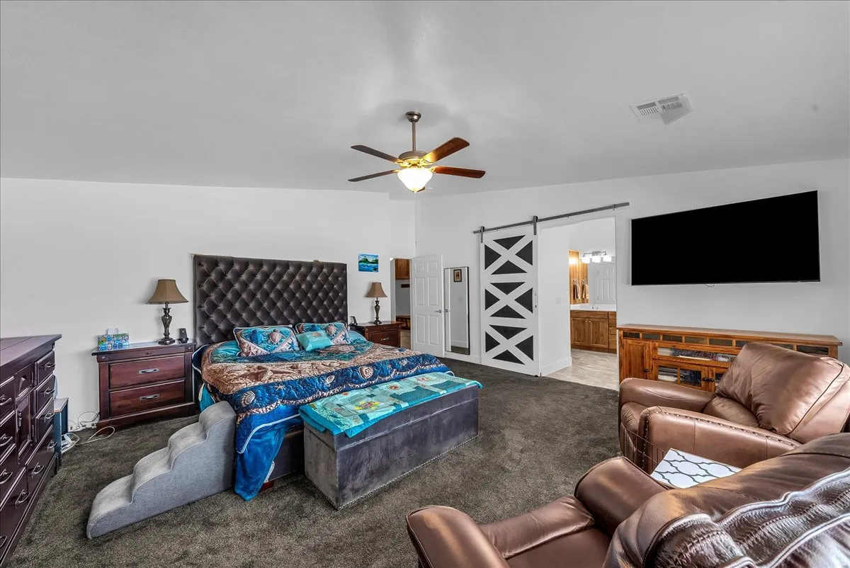 Spacious bedroom featuring dark-toned carpet flooring, a ceiling fan with integrated lighting, and white walls