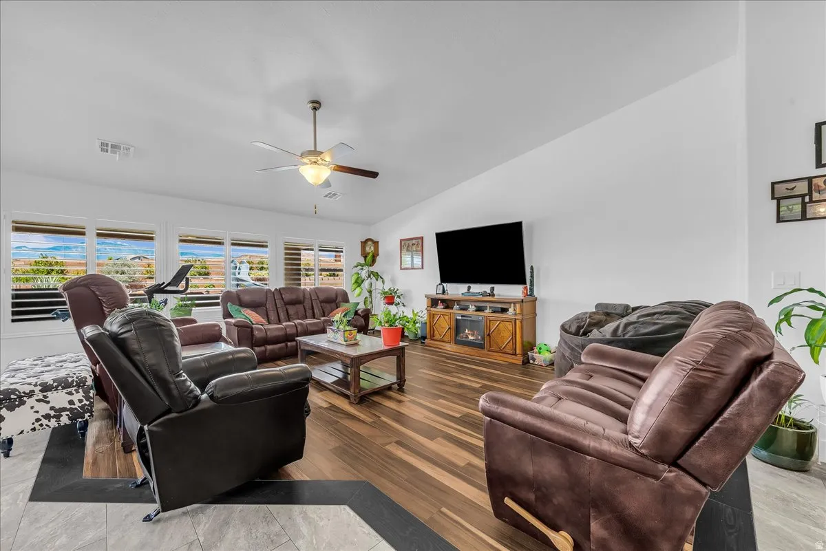 Spacious living area featuring expansive windows with mountain scenery, a ceiling fan, wood-finish flooring, and a built-in media console with an integrated electric fireplace