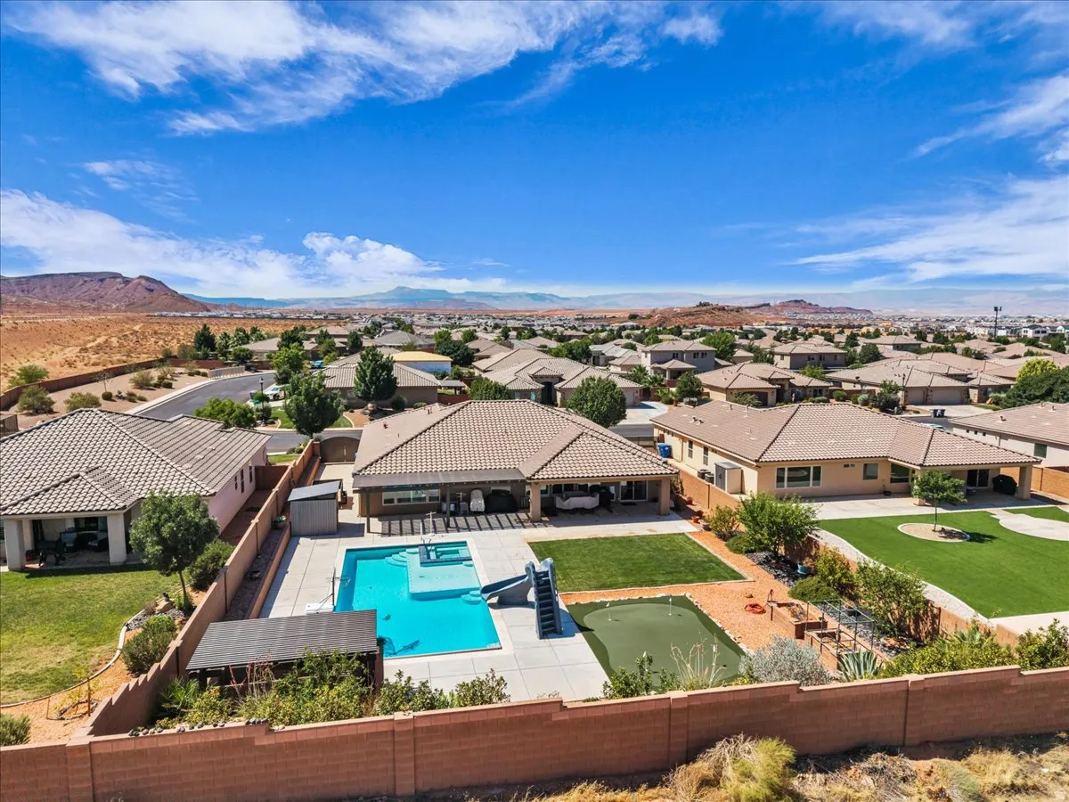 Expansive backyard featuring a rectangular swimming pool with integrated spa and slide, a large concrete patio, and a manicured lawn