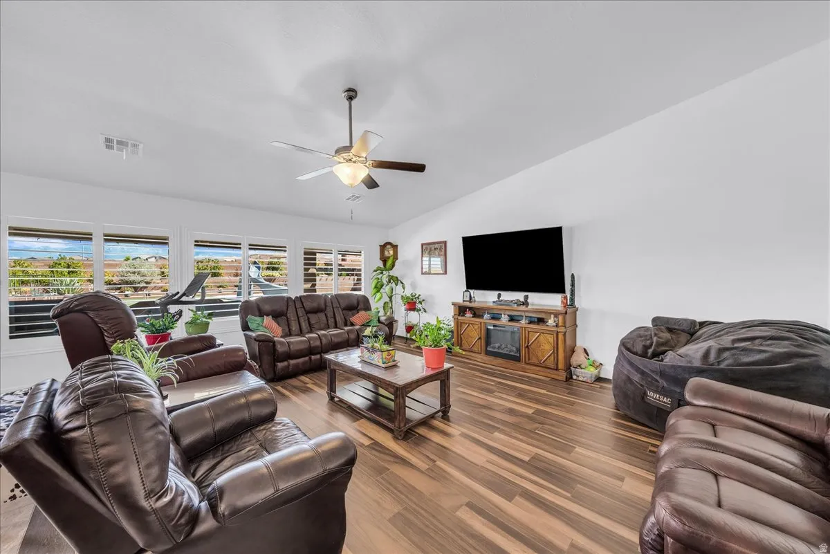 Expansive living area featuring wood-finish flooring, a ceiling fan with integrated lighting, and multiple windows with plantation shutters