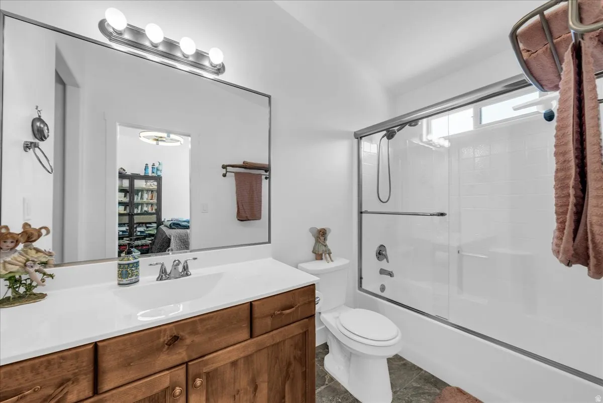 Bathroom featuring a wood-finish vanity with a white countertop, large wall mirror, and a shower-tub combination with sliding glass doors and white subway tile surround