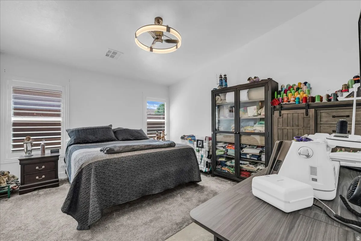 Bedroom featuring light gray carpeting, white walls, and two windows with horizontal blinds