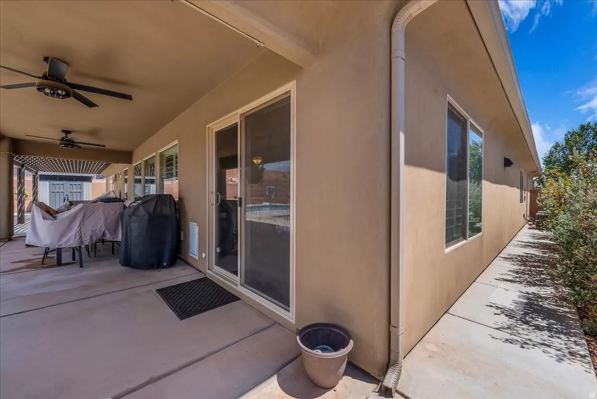 Covered patio with integrated ceiling fans, multiple windows, a sliding glass door, and an extended concrete walkway