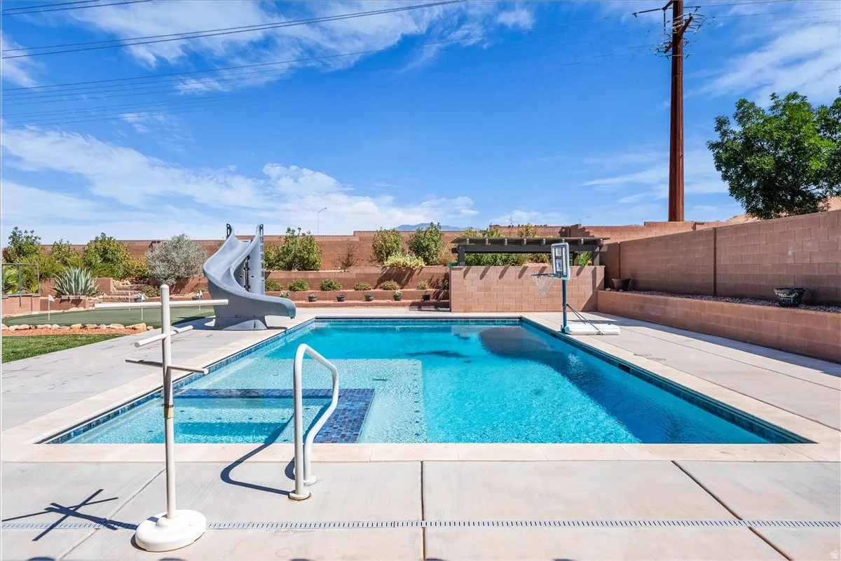 Expansive backyard featuring a rectangular in-ground pool with integrated slide, surrounding concrete patio, and a putting green