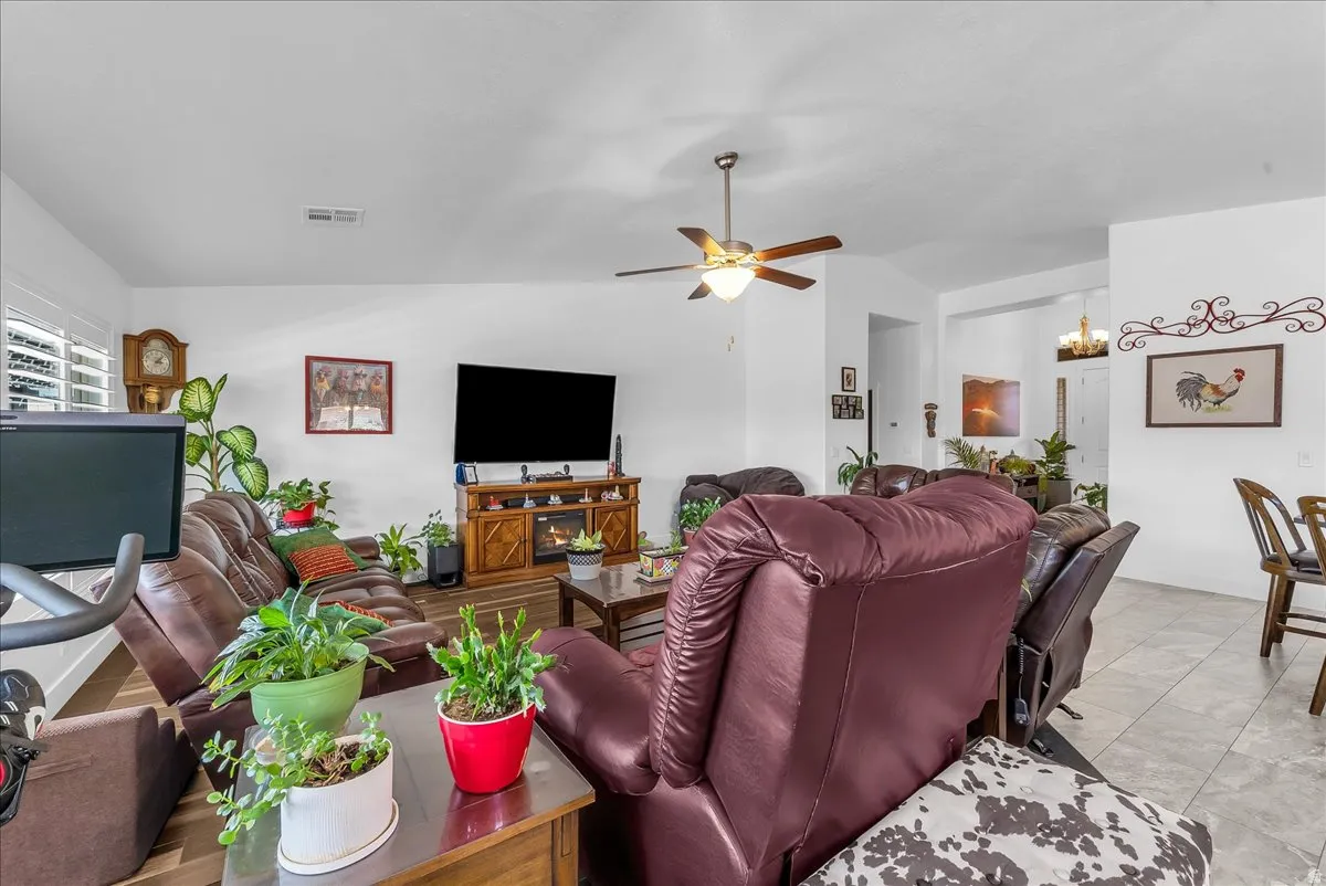 Living area featuring wood-finish flooring, white walls, and a ceiling fan with integrated lighting