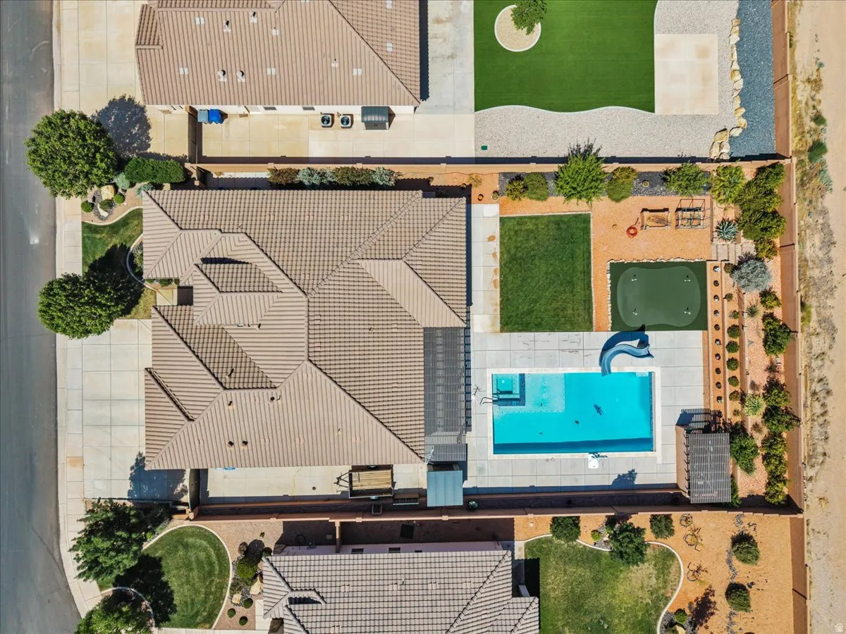 Expansive outdoor area featuring a rectangular swimming pool with an attached slide, a putting green, a separate patch of manicured lawn, and mature desert landscaping with gravel and rock pathways