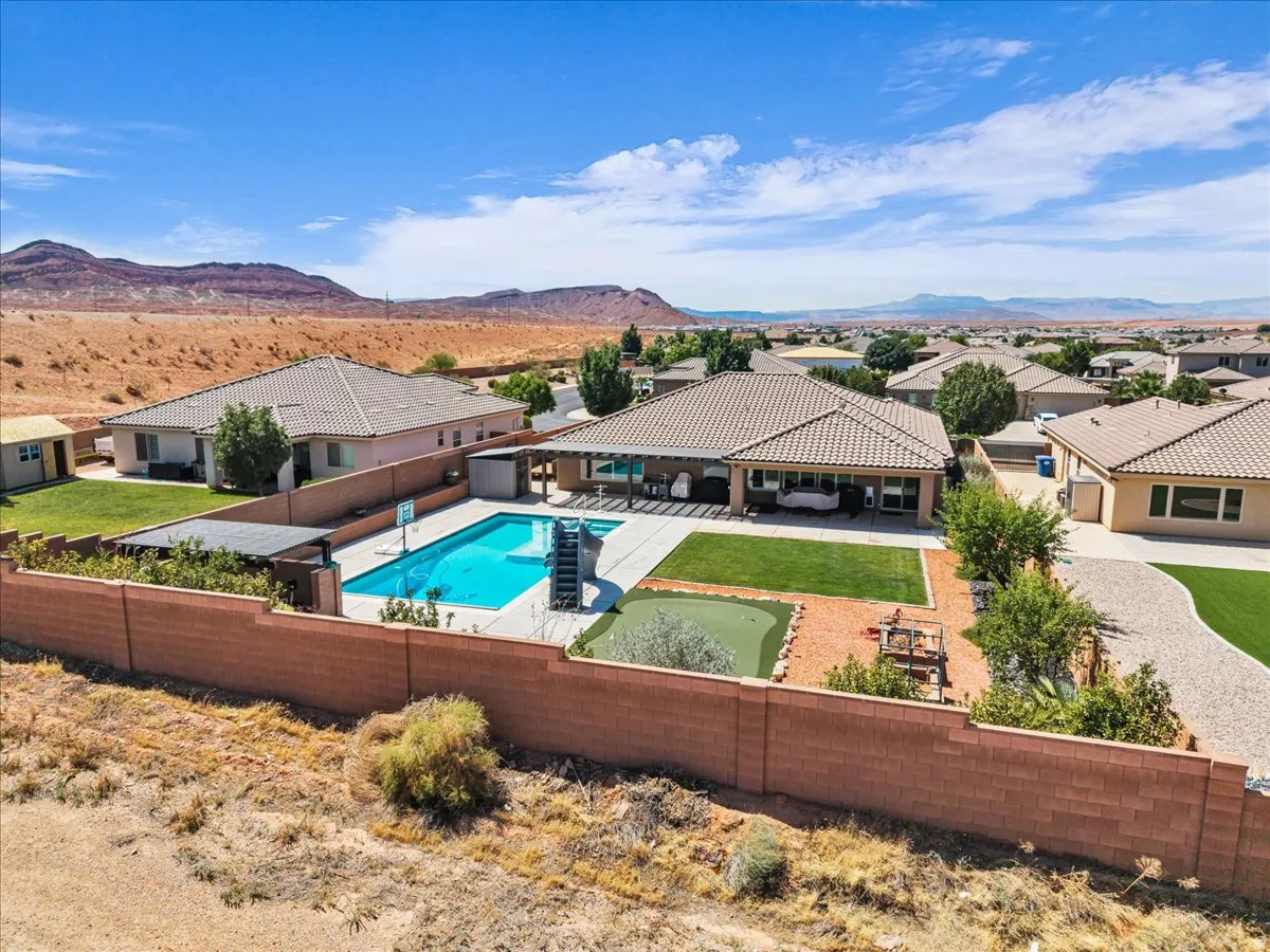 Rear exterior featuring a rectangular pool, covered patio, artificial turf putting green, and desert landscaping