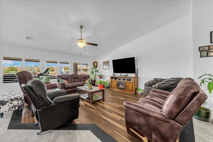 Spacious living area featuring expansive windows with mountain scenery, a ceiling fan, wood-finish flooring, and a built-in media console with an integrated electric fireplace