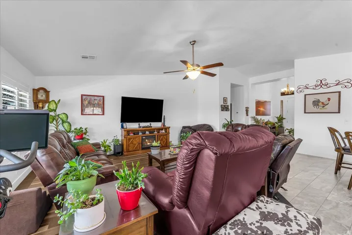 Living area featuring wood-finish flooring, white walls, and a ceiling fan with integrated lighting