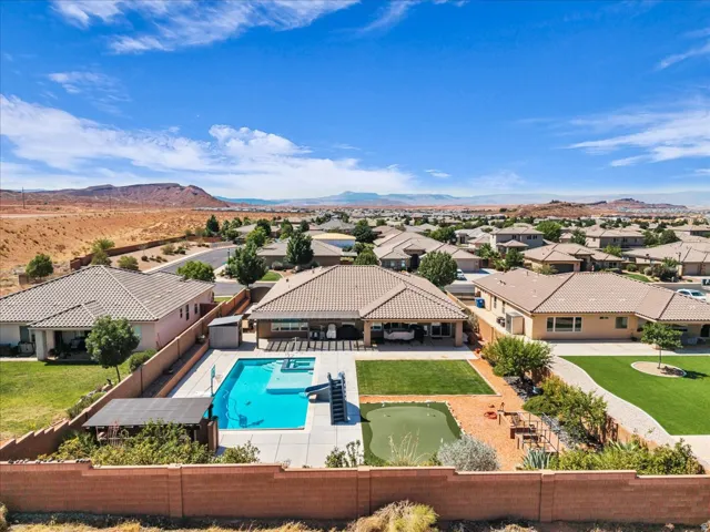 Expansive backyard featuring a large swimming pool, surrounding concrete patio, covered patio, artificial turf lawn, and a putting green