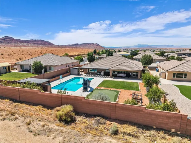 Rear exterior featuring a rectangular pool, covered patio, artificial turf putting green, and desert landscaping