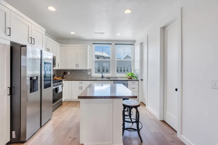 Contemporary kitchen featuring white cabinetry, stainless steel appliances, a center island with a dark countertop, wood-finish flooring, and recessed lighting