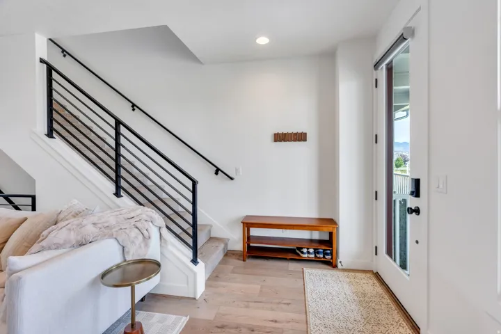 Entryway featuring wood-finish flooring, a contemporary staircase with black metal railings, a recessed ceiling light, and a white entry door with frosted glass