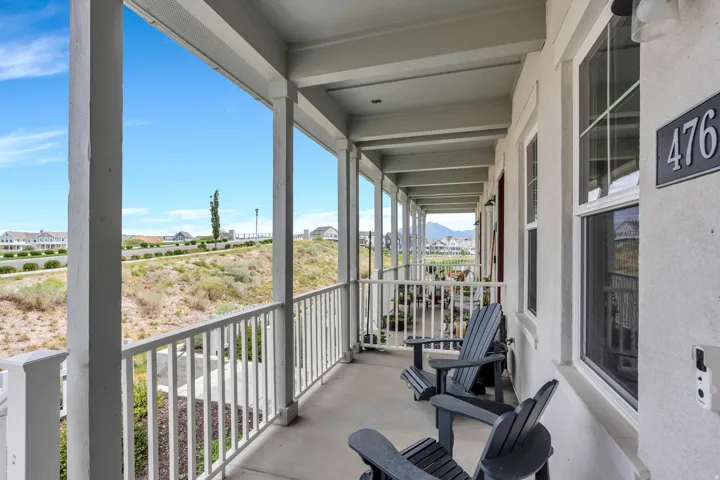 Covered balcony with white railing, featuring exterior stucco finish and multiple windows