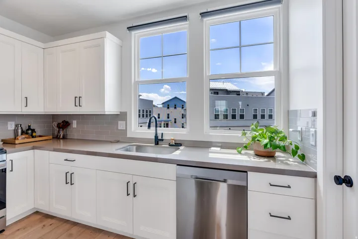Kitchen featuring white shaker-style cabinetry, a stainless steel sink with a matte black faucet, light grey countertops, a subway tile backsplash, and wood-finish flooring