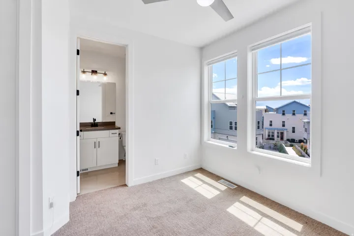 Carpeted room with white walls, featuring two large windows and a ceiling fan