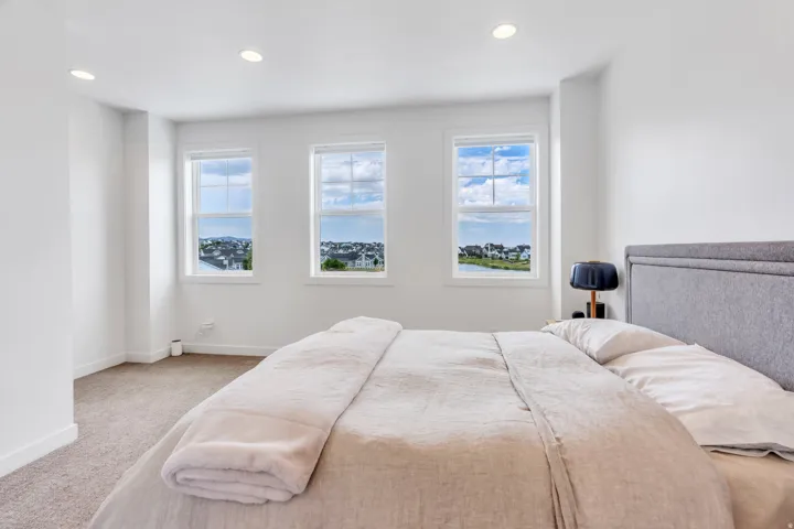 Bright bedroom featuring white walls, recessed ceiling lighting, three windows, and carpet flooring