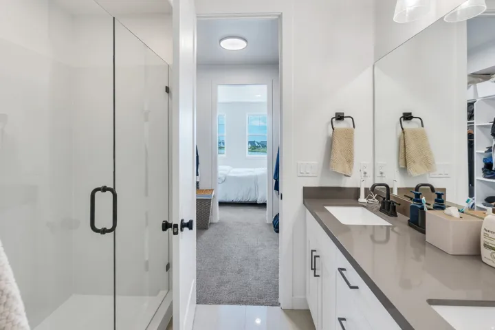 Bathroom featuring a glass-enclosed shower, dual vanity with undermount sinks, stone countertops, and dark-finish fixtures