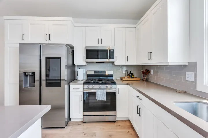 Modern kitchen featuring white shaker-style cabinetry, stainless steel appliances, light-toned countertops, a subway tile backsplash, and wood-finish flooring