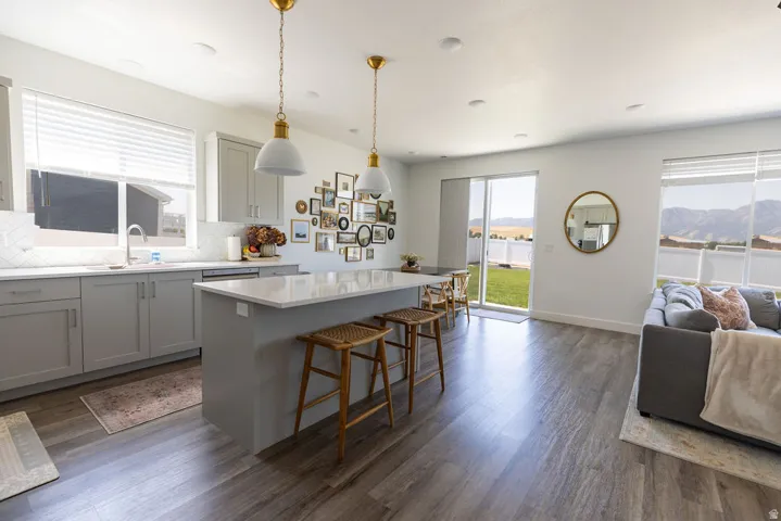 Open-concept living space featuring wood-finish flooring, a kitchen island with seating, light gray cabinetry, white countertops, and a sliding glass door opening to a green lawn