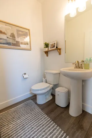 Bathroom featuring a pedestal sink, brushed brass faucet, wood-finish flooring, and a wall-mounted light fixture with three sconces