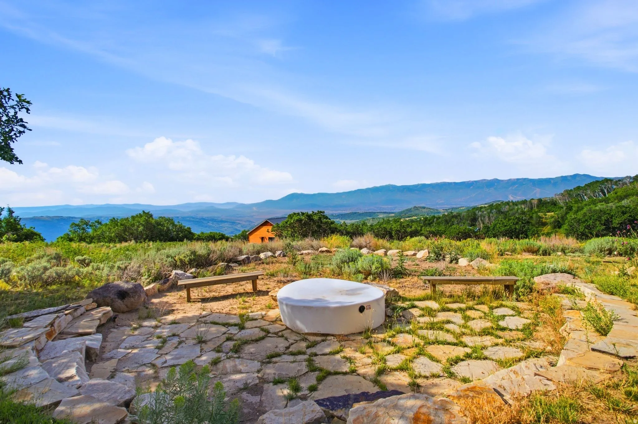 Stone patio area featuring a propane fire pit, surrounded by two wooden benches and additional stone seating