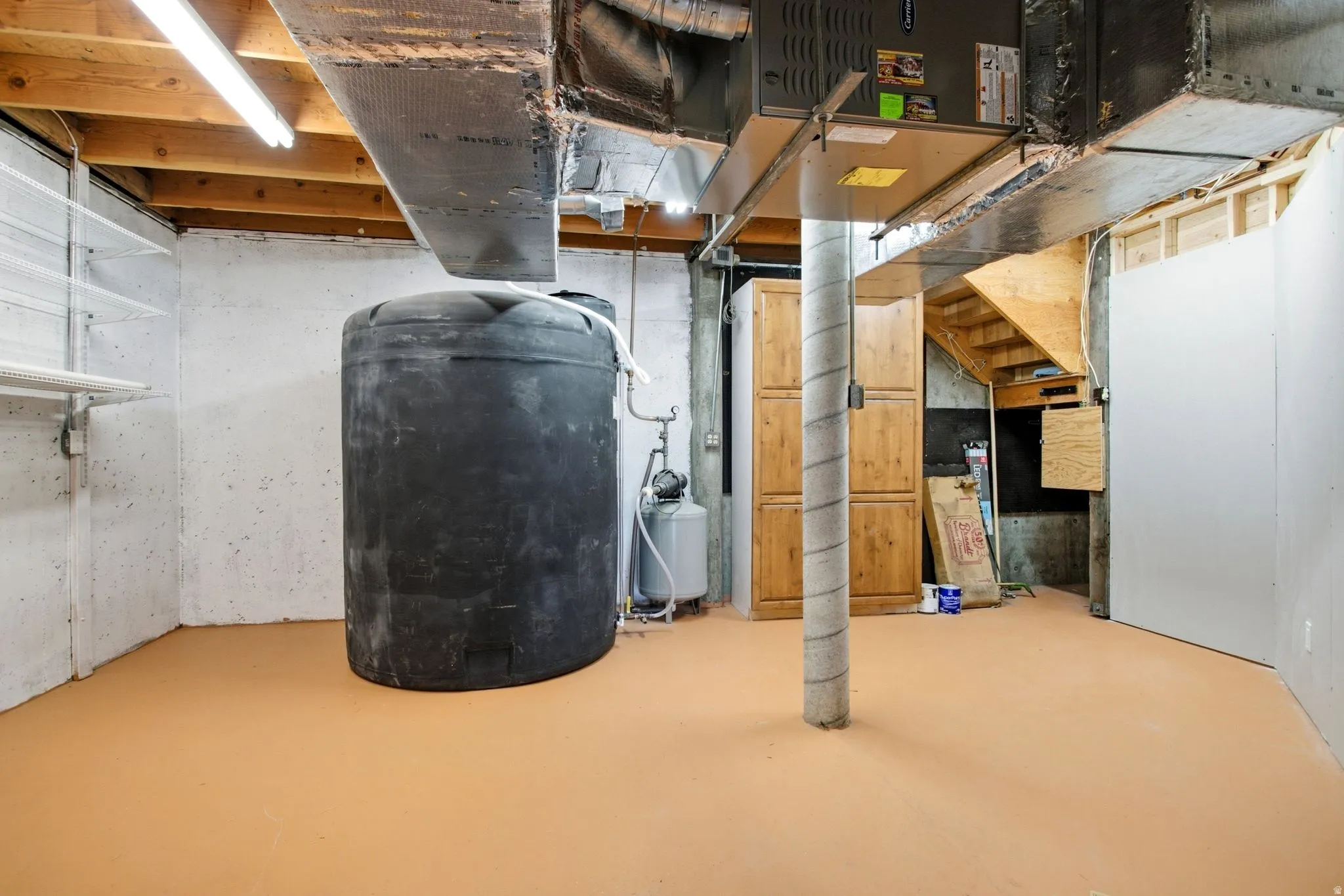 Unfinished basement space featuring emergency back up water tank, safe, exposed ductwork, concrete flooring, massive storage cupboards and a visible staircase