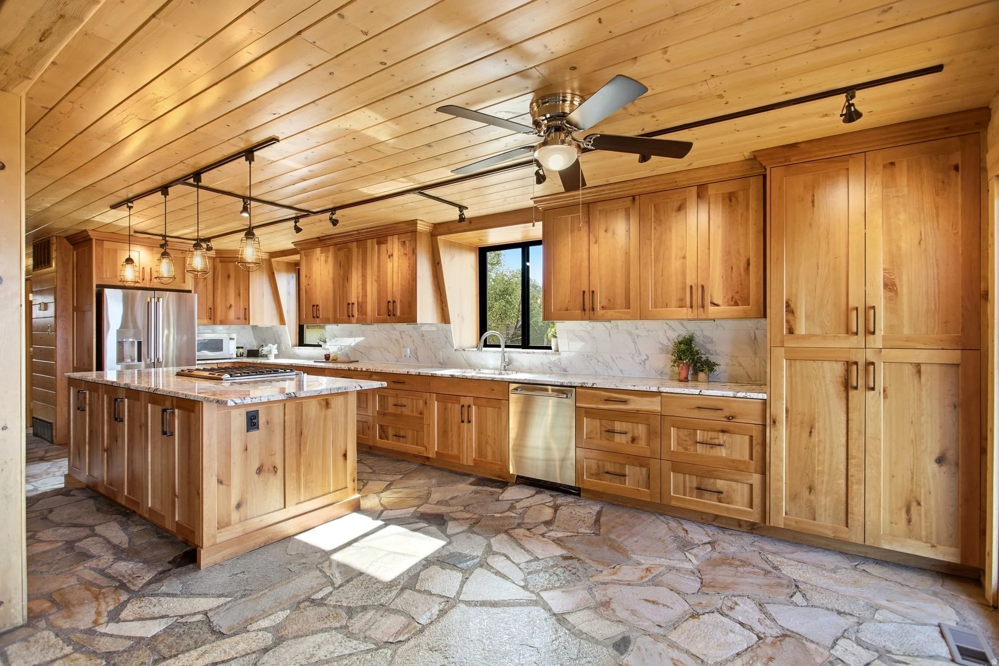 Kitchen featuring extensive wood cabinetry, stone slab countertops, stainless steel appliances, a center island, and a natural flagstone floor