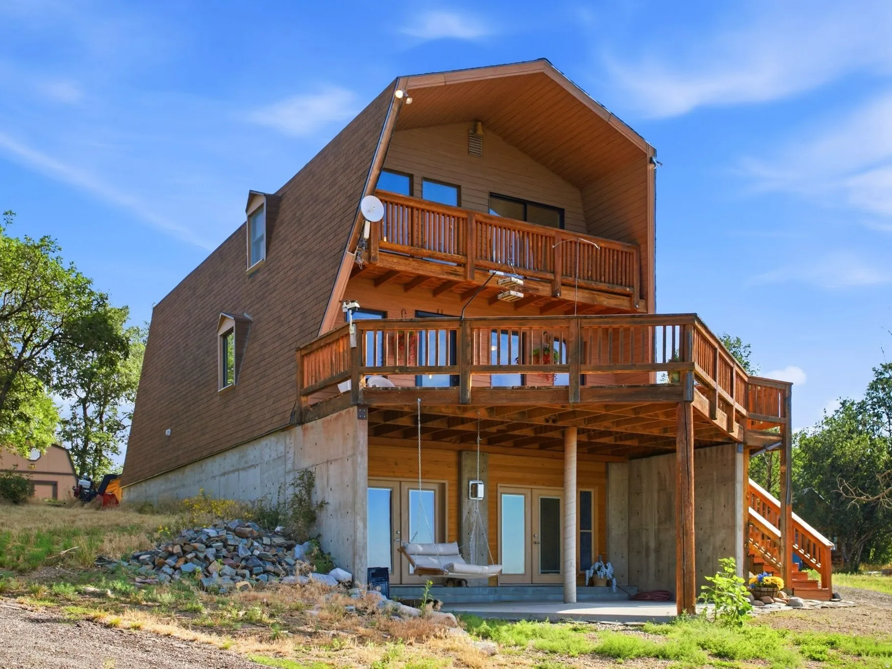 Gambrel-style residence featuring multiple wood-finish decks, shingled roofing, and a concrete foundation
