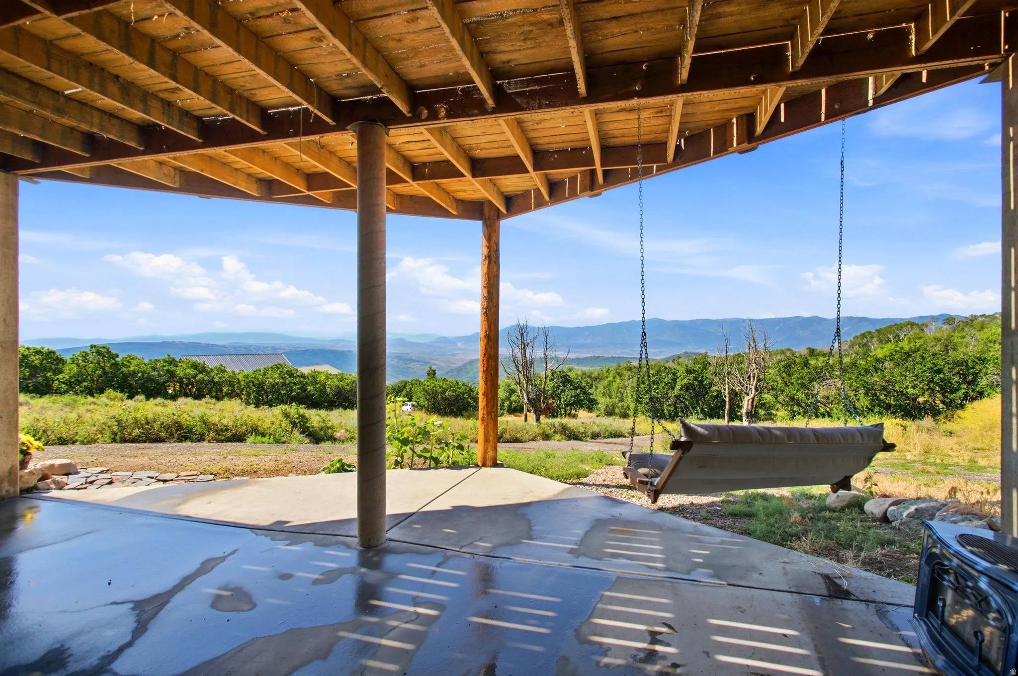 Covered concrete patio with exposed wood joist ceiling, supported by rustic posts