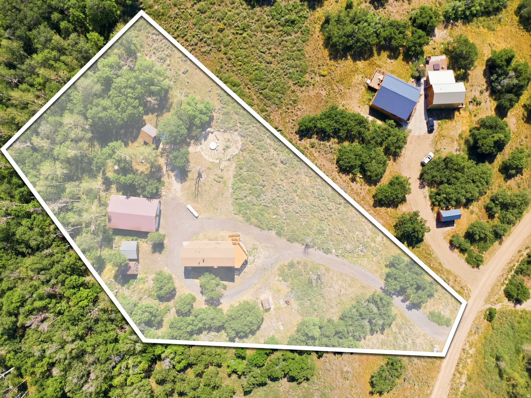 Expansive property featuring multiple structures, including two primary buildings with distinct roofing, surrounded by natural vegetation