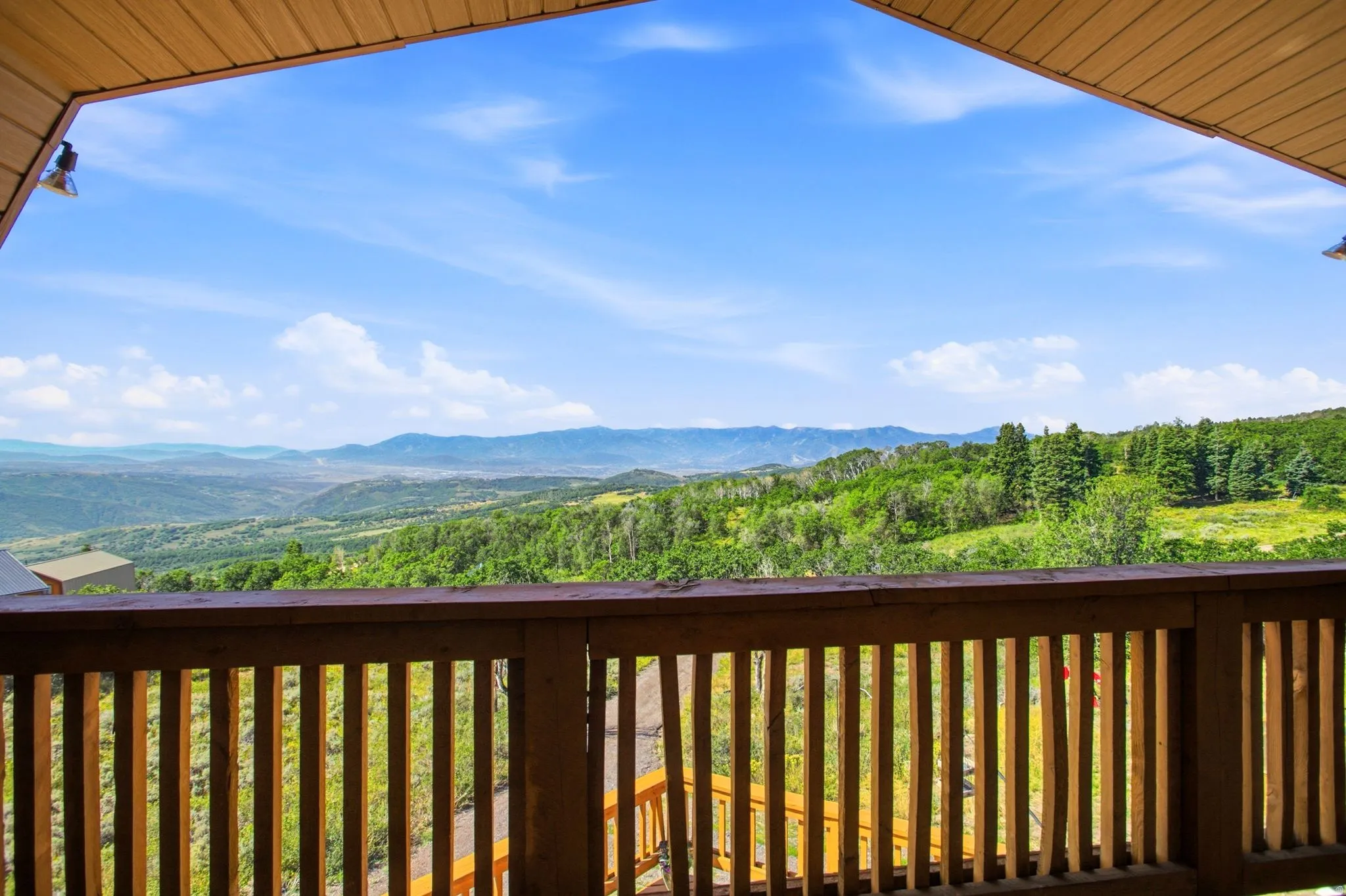 Expansive outdoor deck with natural wood railing overlooking a distant mountain range and verdant tree-covered hillsides
