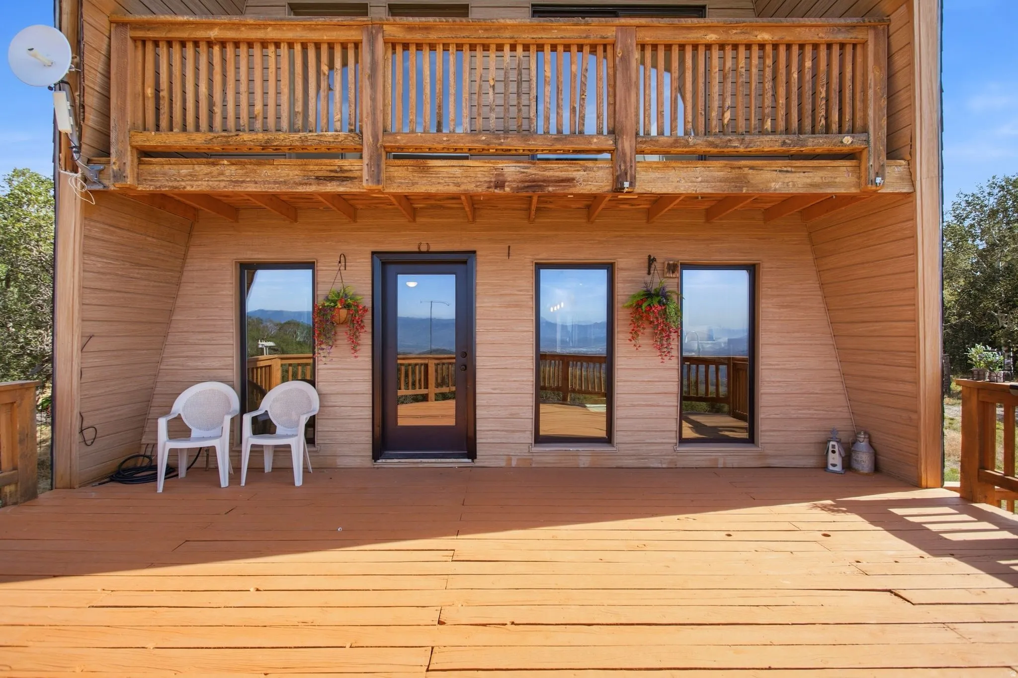 Expansive wood deck with a full-light entry door and three windows, featuring a wood-plank exterior and an upper-level wood balcony