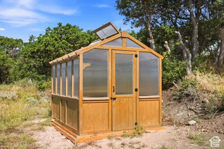 Freestanding wooden greenhouse featuring a pitched roof, translucent paneling, and a single entry door with dark hardware