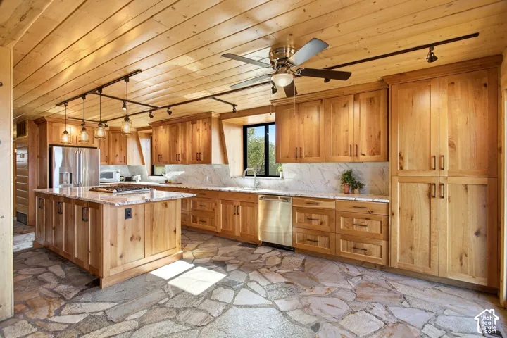 Kitchen featuring extensive wood cabinetry, stone slab countertops, stainless steel appliances, a center island, and a natural flagstone floor