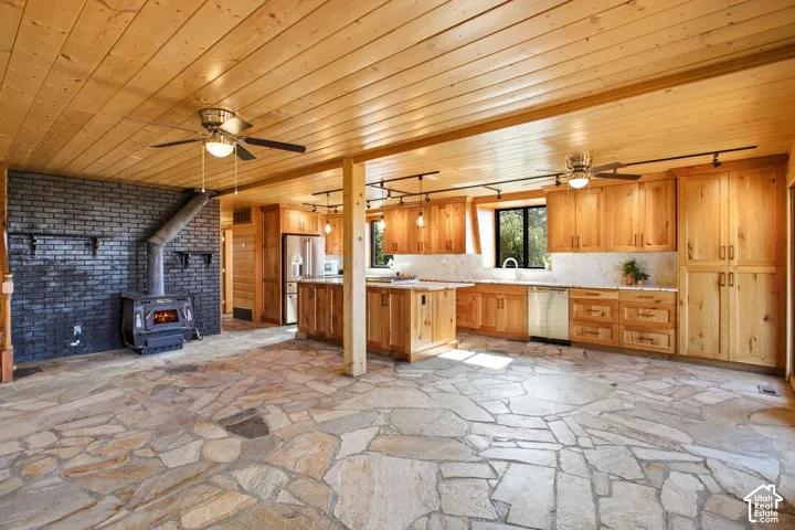 Open-concept living space with flagstone flooring, wood plank ceilings, and a black brick fireplace featuring a wood-burning stove