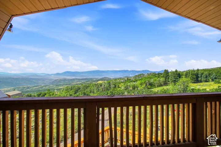 Expansive outdoor deck with natural wood railing overlooking a distant mountain range and verdant tree-covered hillsides