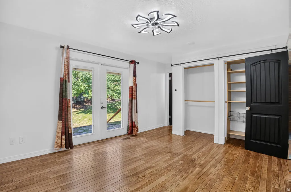 Hardwood-finish flooring throughout, featuring french doors with exterior access, a contemporary ceiling fixture, and a closet with built-in shelving