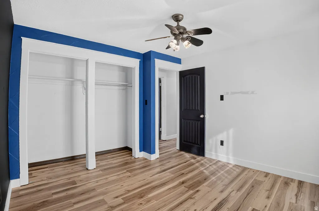 Room featuring wood-finish flooring, a ceiling fan with integrated lighting, and a white baseboard trim