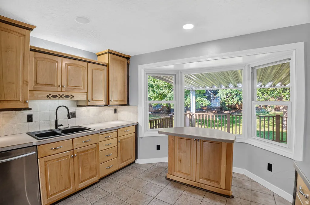 Kitchen featuring wood cabinetry, a stainless steel dishwasher, and a bay window overlooking a deck and backyard