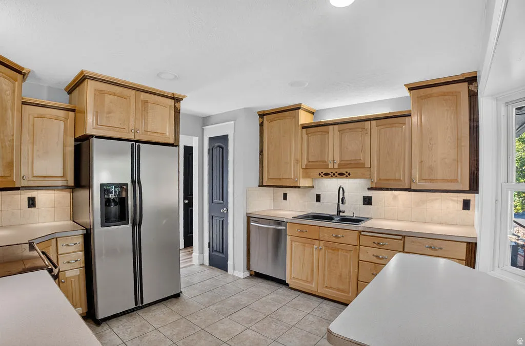 Kitchen featuring light wood cabinetry, stainless steel appliances, tile flooring, and a tiled backsplash