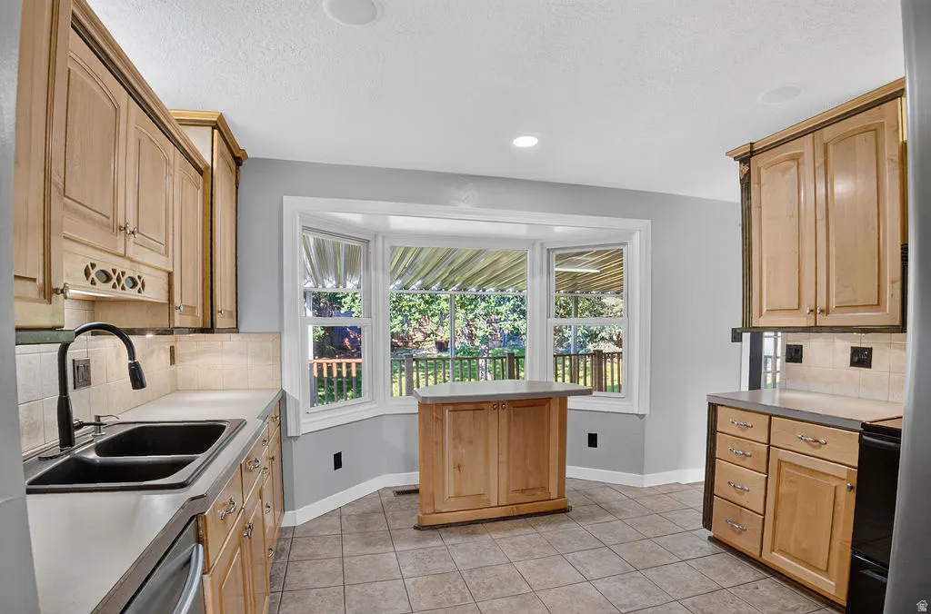 Kitchen with light wood cabinetry, a bay window, tile flooring, and a freestanding island