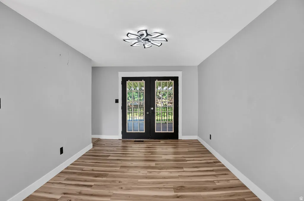 French doors with transom window and decorative grilles, wood-finish flooring, contemporary ceiling fixture, white trim, and neutral wall tones