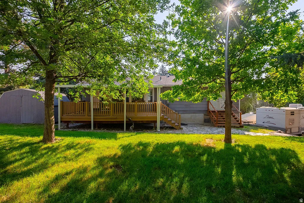 Rear exterior featuring a spacious wood deck with white posts, a separate exterior staircase, and mature trees providing natural shade