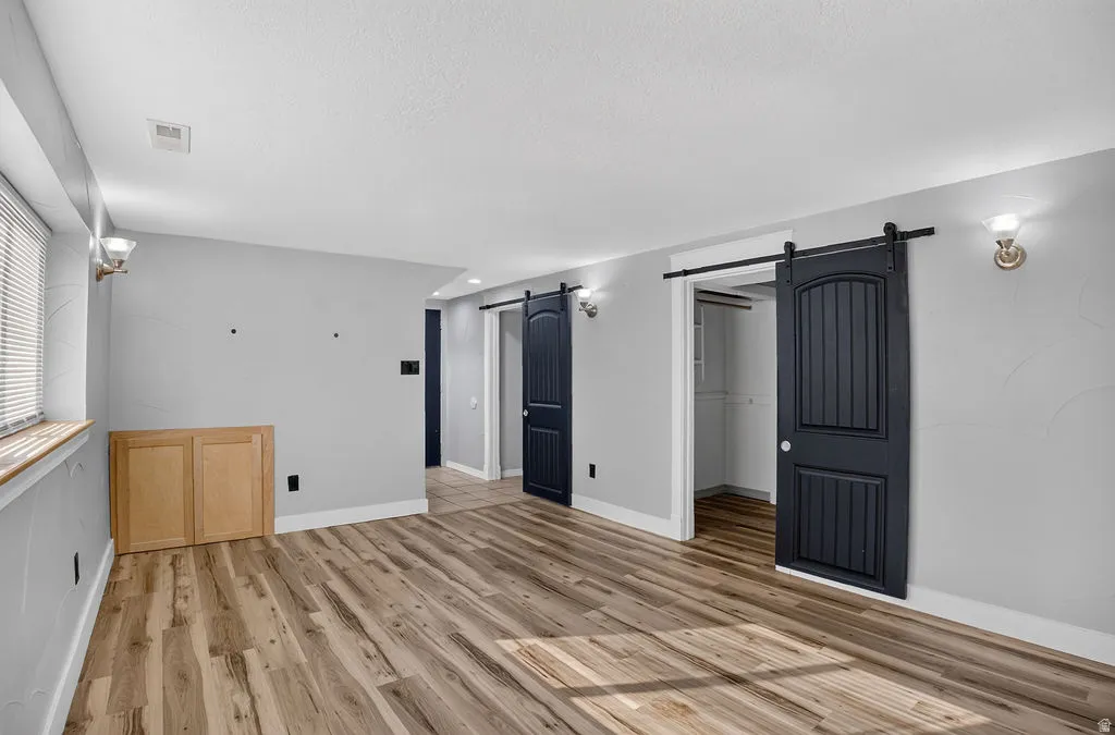 Spacious room featuring wood-finish flooring, light grey walls, and two dark paneled barn doors with exposed hardware