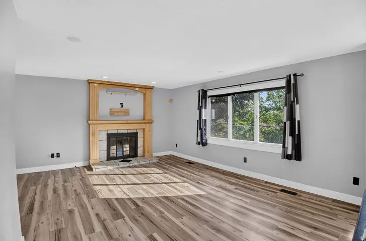 Spacious room featuring wood-finish flooring, a stone-faced fireplace with a wood mantel, and large windows with white trim